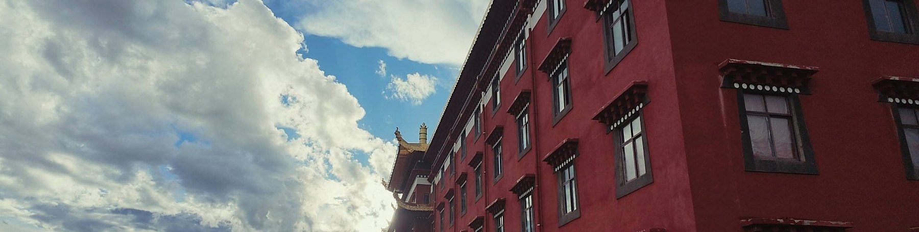 Mur rouge et toit doré d'un monastère, nuages et montagne à gauche