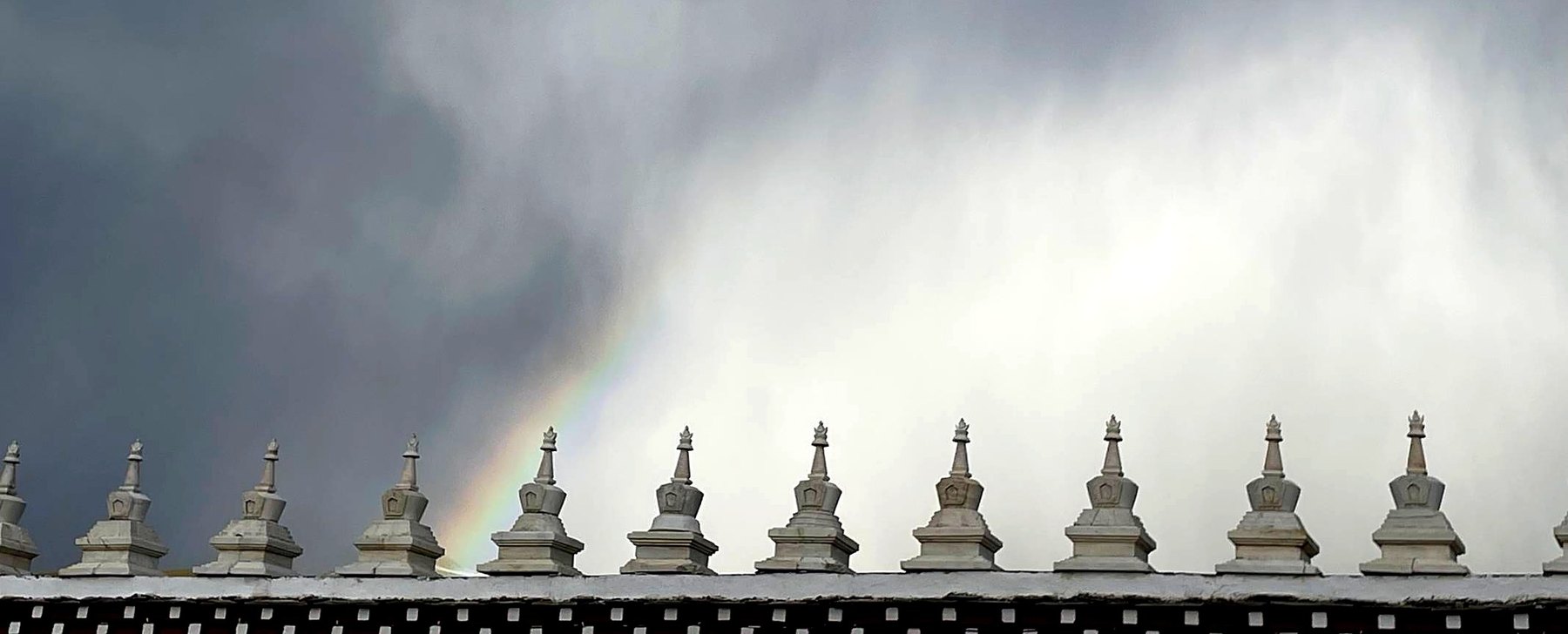 Rangée de petits stupas au bord d'un toit de monastère, arc-en-ciel pâle dans le ciel après la pluie
