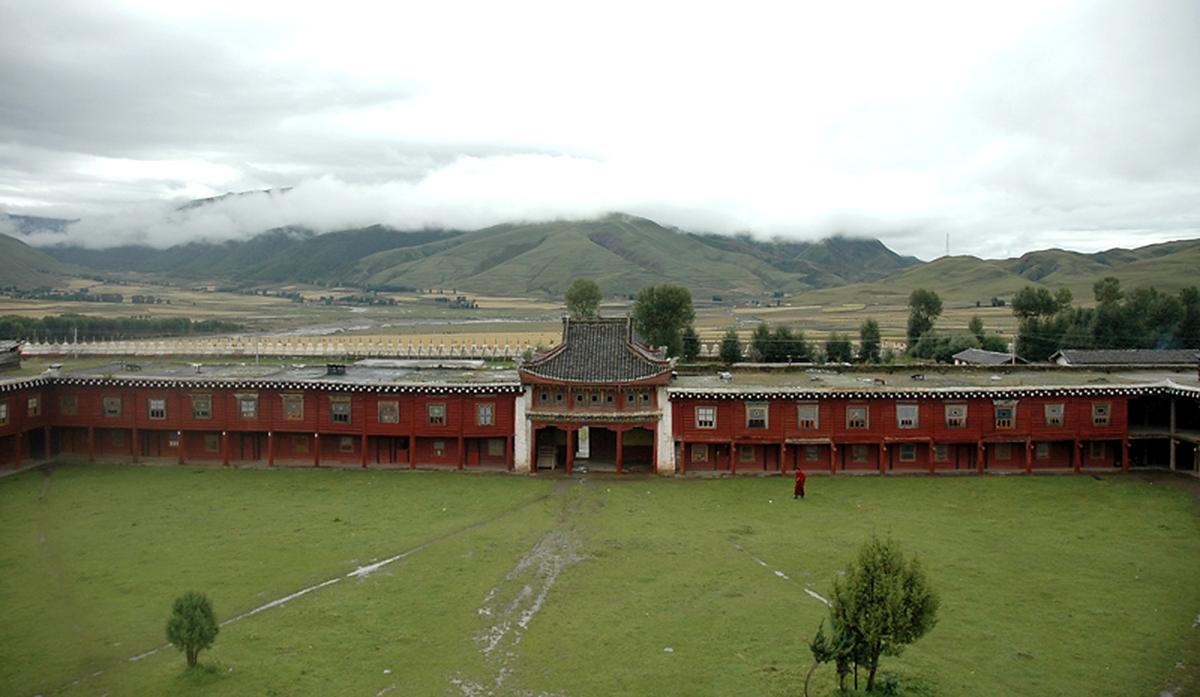 Huiyuan monastery: a red perimeter wall with a Chinese-roofed gate in the middle, a lawn in front, white stupas and fields beyond