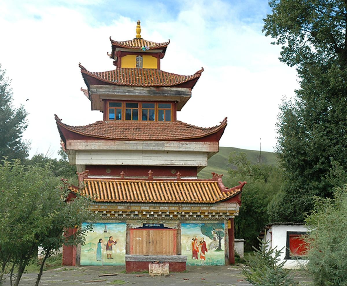 A three-tiered pavilion with Chinese tiled roofs and a gilded finial, murals at ground level, among old trees