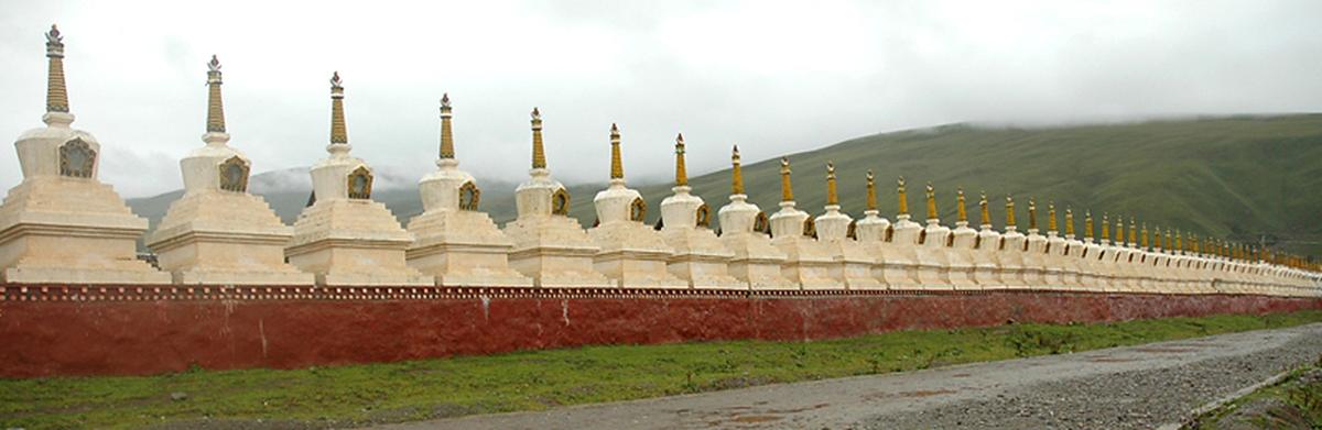 A long row of white stupas standing on a red wall, running away to the right