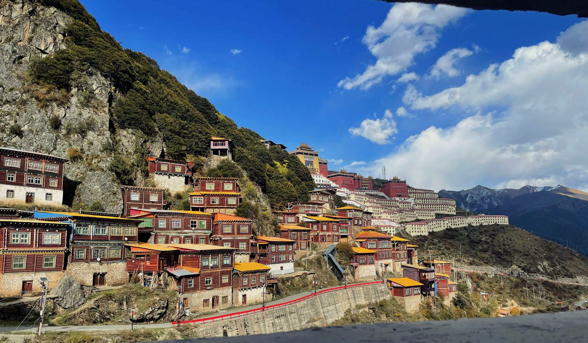 從廁所窗口往外看:一排木牆平房、一道紅欄杆、坡上的大殿與遠山
