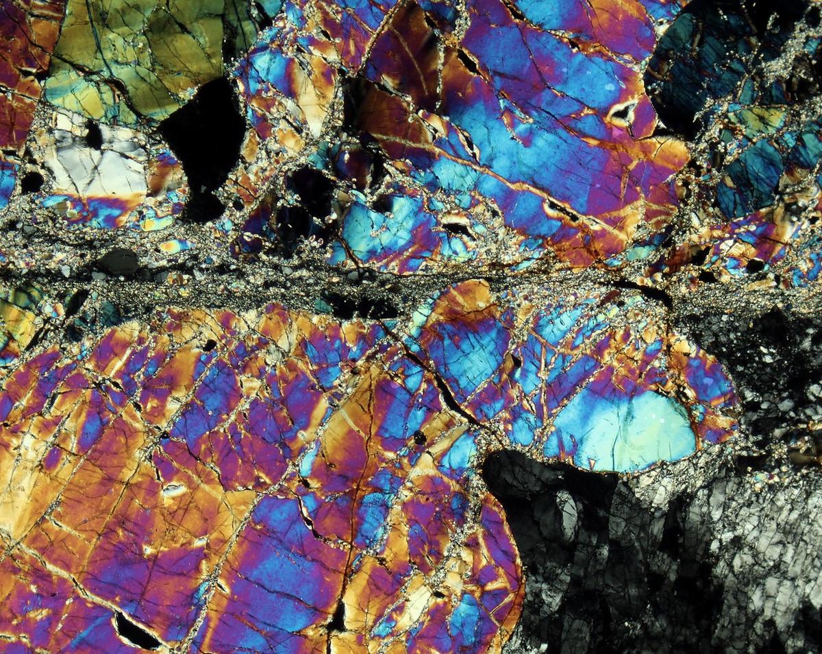 Photomicrograph of mylonite under crossed polarisers: a dark shear band cutting across a mosaic of brightly coloured mineral grains