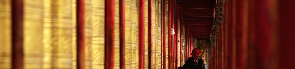 The prayer-wheel corridor at Tagong monastery, a monk walking between rows of gilded wheels