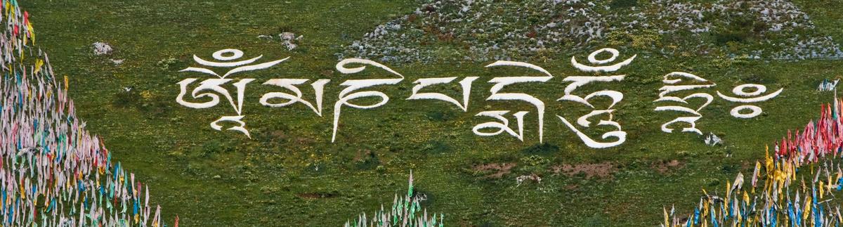 A hillside with the six-syllable mantra built in white stone, surrounded by prayer-flag arrays