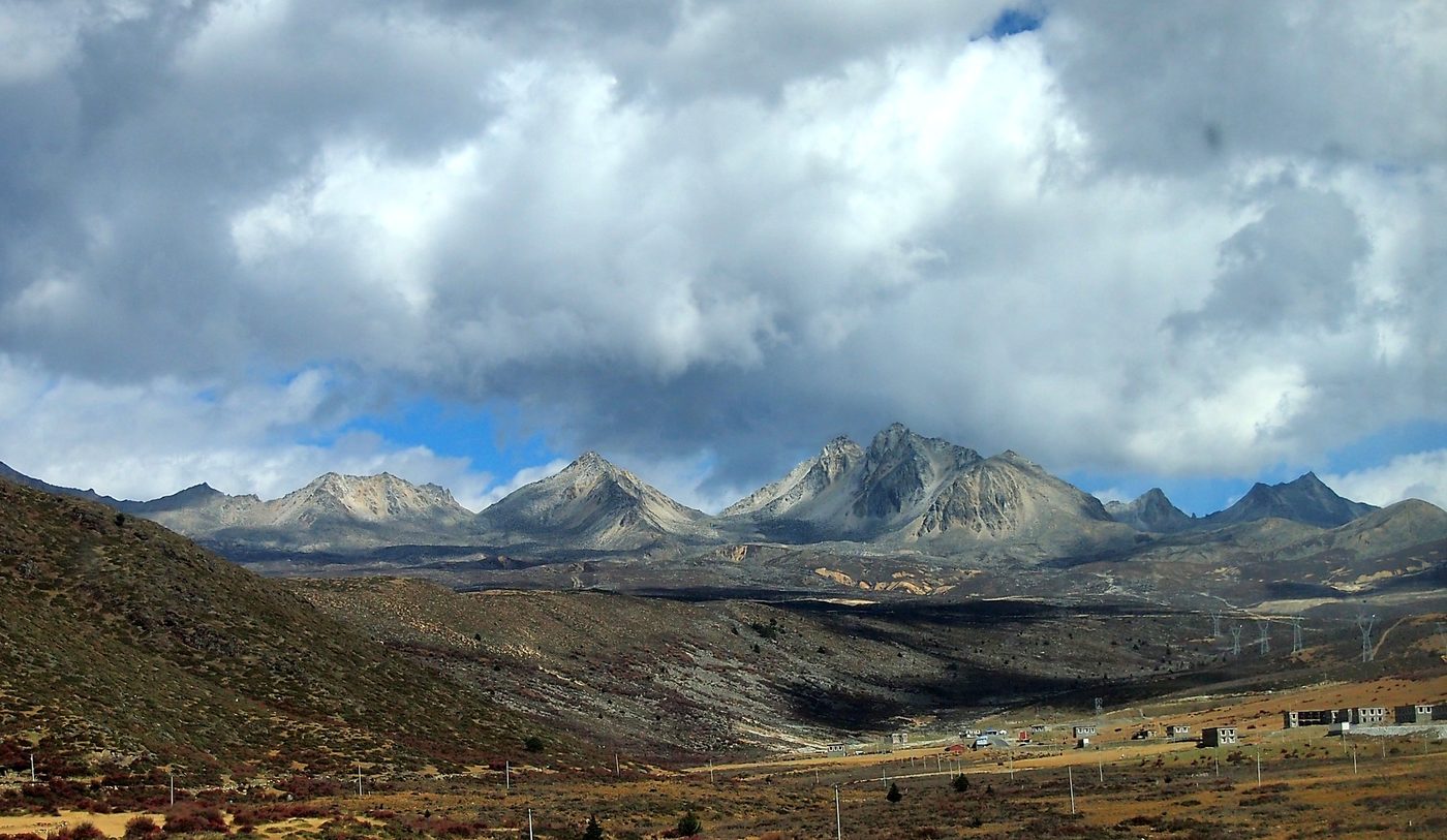 A high pass in western Sichuan: grass and gravel in the foreground, a snow ridge under heavy cloud