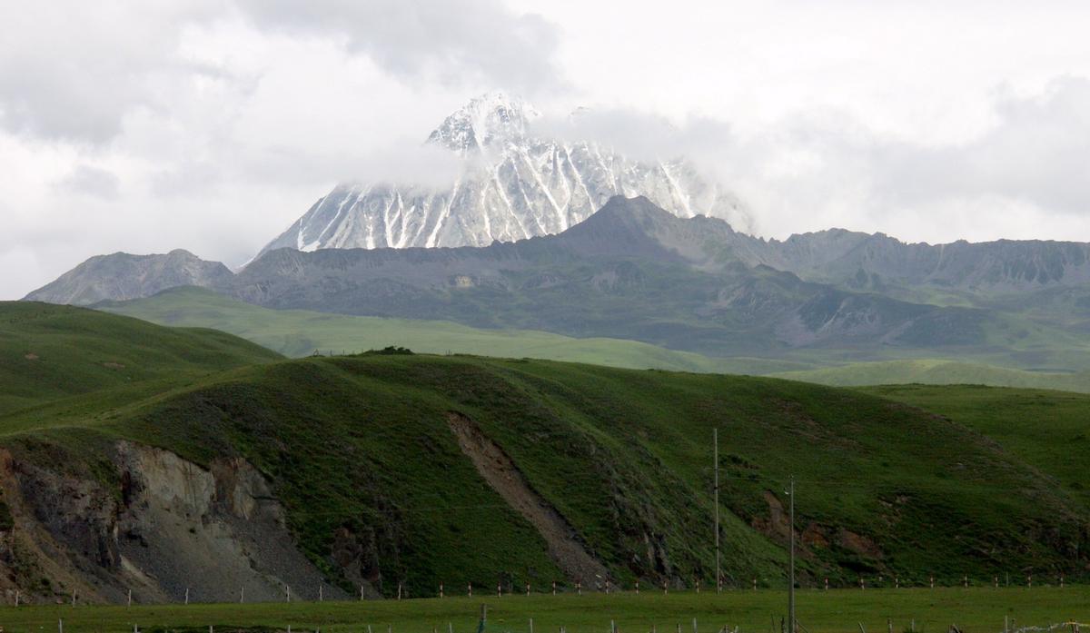 Yala / Haizi Shan seen across grassland, its summit under cloud